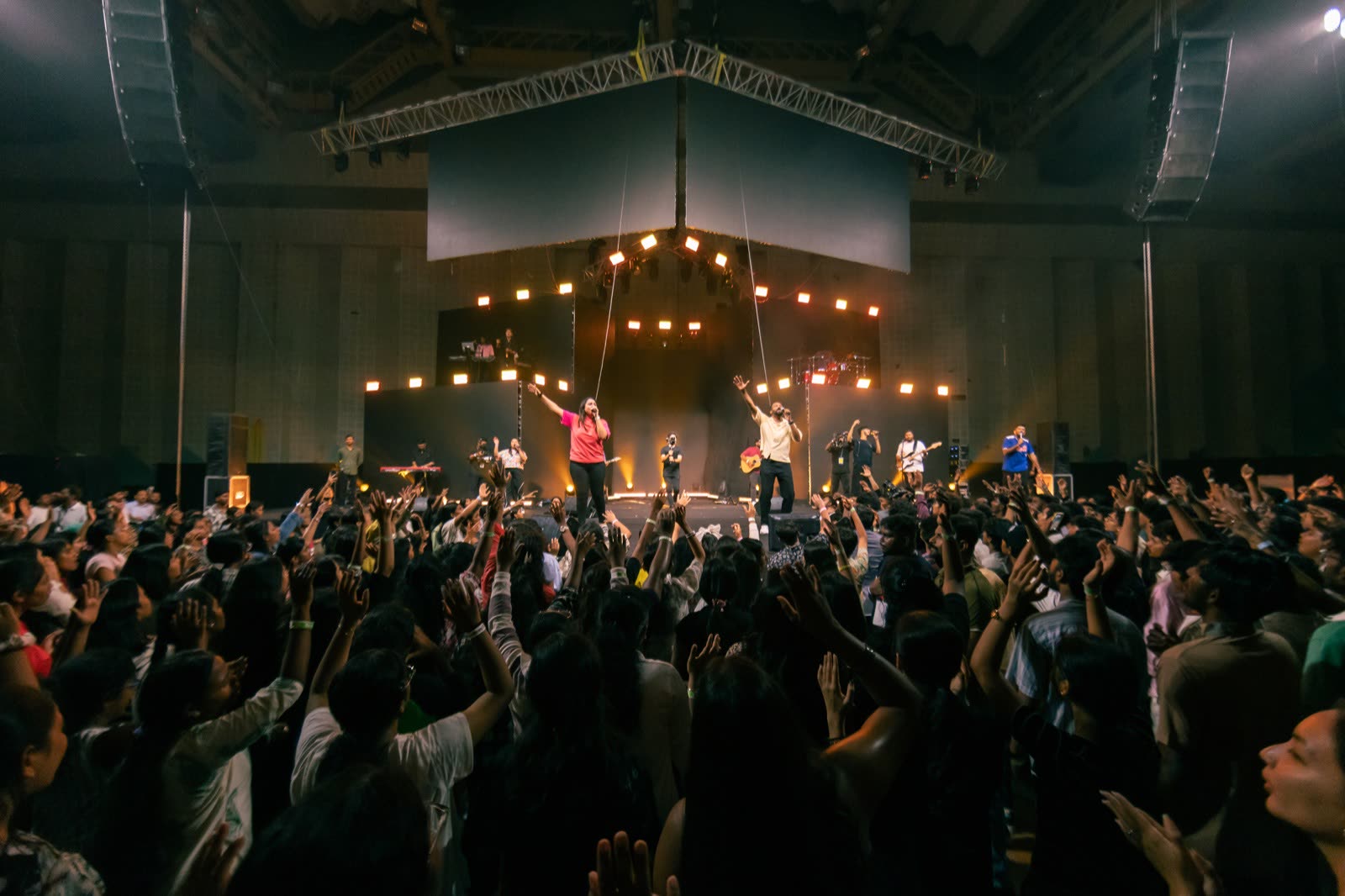 Crowd with hands raised facing a worship band under warm lights